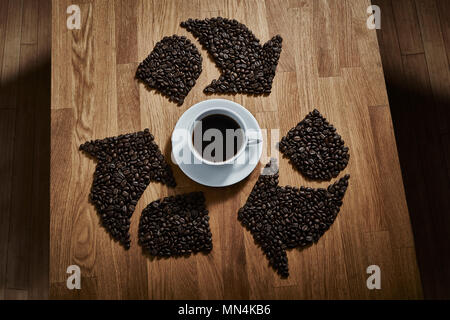 I chicchi di caffè formando simbolo di riciclaggio intorno a tazza da caffè Foto Stock