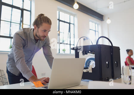 Maschio di designer che lavora al computer portatile accanto alla stampante 3D in office Foto Stock