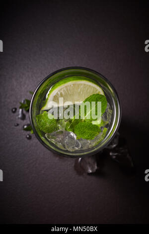 La tradizione bevanda estiva mojito con lime e menta in vetro scuro su sfondo di pietra Foto Stock