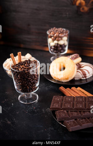 Vetro con i chicchi di caffè accanto a tavolette di cioccolato, ciambelle, lo zucchero di canna e di altro vetro con arachidi in cioccolato Foto Stock