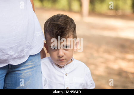 Shy boy in piedi con la sua madre all'aperto Foto Stock