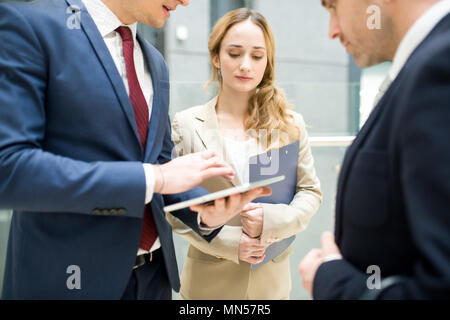 Vita ritratto di tre aziende moderne persone per discutere il lavoro in piedi in edificio di uffici, concentrarsi sulla bella donna bionda Foto Stock