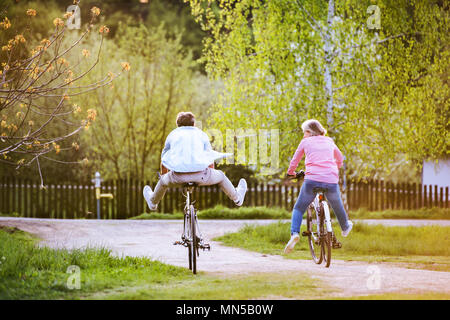 Bella coppia senior con biciclette ciclismo fuori in primavera la natura, divertendosi. Vista posteriore. Foto Stock