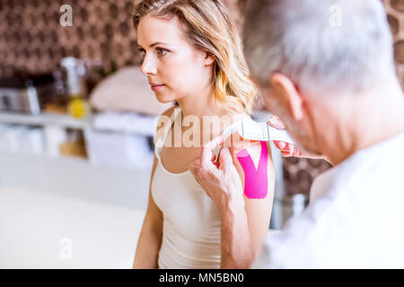 Un irriconoscibile fisioterapista maschio con l'applicazione del nastro su un giovane paziente femmina. Close up. Foto Stock