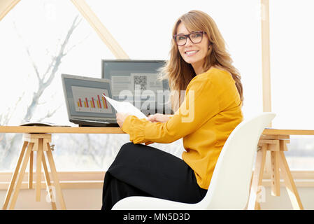 Persone di mezza età manager finanziario imprenditrice seduti nella parte anteriore del notebook e computer e facendo alcuni documenti. Foto Stock