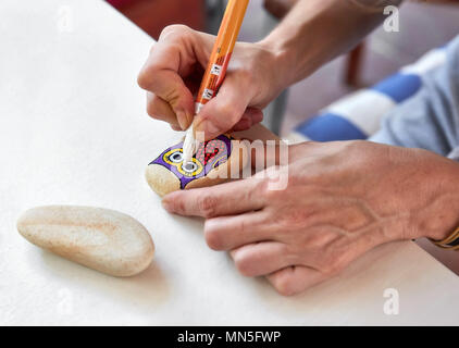 La donna caucasica pittura un gufo su una pietra. Vernice di pietra hobby, arti e mestieri. Foto Stock