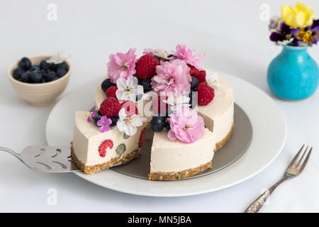 Una fetta di casalinghe cheesecake vegan per dessert. Decorate con lamponi mirtilli freschi e fioriture primaverili. Foto Stock