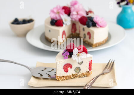 Una fetta di casalinghe cheesecake vegan per dessert. Decorate con lamponi mirtilli freschi e fioriture primaverili. Foto Stock