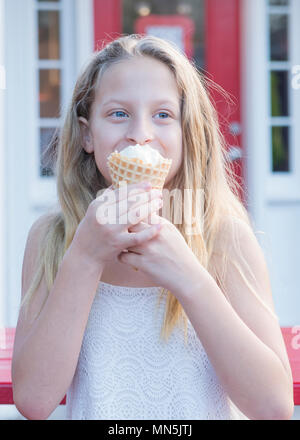 10 anno vecchia ragazza con lunghi capelli biondi godendo di un cono gelato. Immagine viene dalla vita in su. Foto Stock