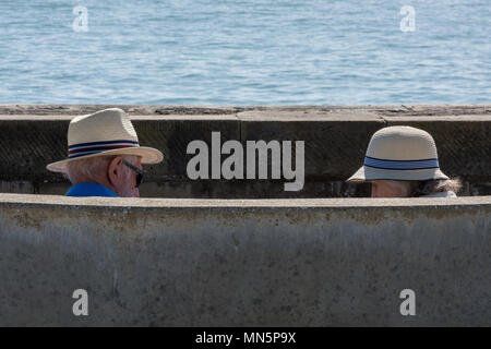 Due persone anziane marito e moglie in pensione e seduta su una panchina in riva al mare indossando tradizionalmente British Panama cappelli per proteggersi dal sole. Foto Stock