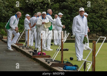 Un certo numero di anziani pensionati signori prato giocando a bocce su un bowling green vestito in bianchi. Foto Stock