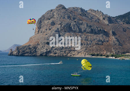 Il parasailing turisti dell'isola di Rodi con vedute del monte Tsambika (Grecia). Due paracaduti-uno con la scritta 'Rodi' in Inglese, e t Foto Stock