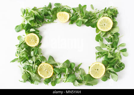 Verde decorativo vegetale composizione del telaio. Varie foglie di insalata. La rucola, rucola, mais con insalata di limoni a fettine isolato su bianco sullo sfondo di legno. Cibo sano sfondo, piana, laici vista superiore Foto Stock