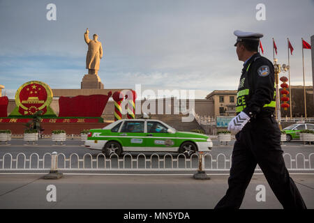 Un poliziotto cinese cammina per la strada davanti a un enorme monumento a Mao Zedong nella città di Kashgar, Xinjiang Uygur regione autonoma della Cina Foto Stock