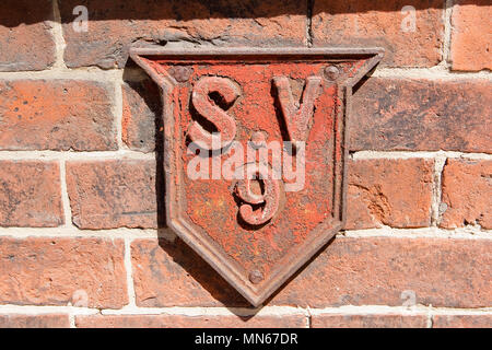 Vecchio weathered red metal services punto firmare in una forma di schermo su uno sfondo in muratura Foto Stock