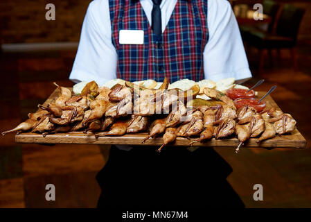Un mucchio di quaglie fritte su una tavola di legno nelle mani di un cameriere. Foto Stock