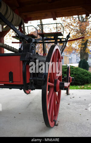 Grande,rosso ruota in legno dal vecchio camion dei pompieri statua nel parco|autunno Foto Stock