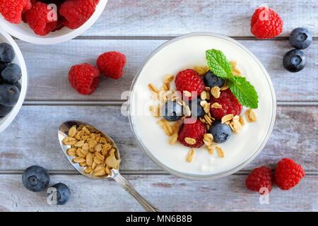Lo yogurt greco con i dolci di bacche e granola, overhead di scena sul legno rustico Foto Stock