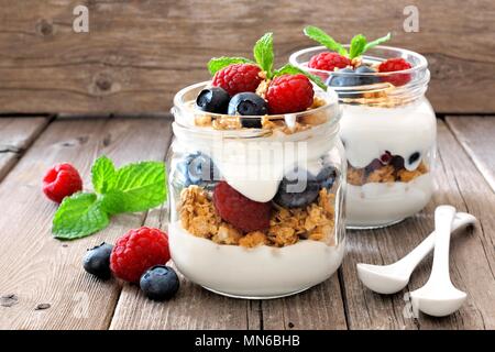 Mirtillo e lampone parfaits in vasetti di vetro, ancora la vita contro un rustico sfondo legno Foto Stock
