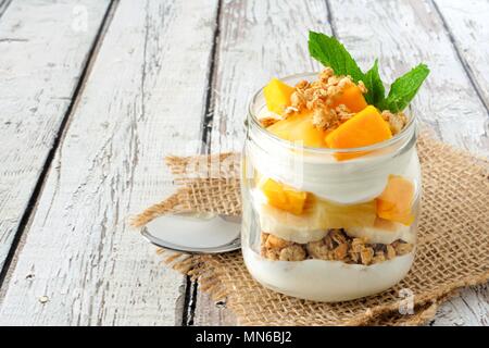 Tropical mango e ananas parfait in un mason jar su un rustico di legno bianco sullo sfondo Foto Stock