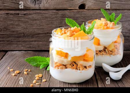 Una sana mango e ananas parfaits in vasetti di vetro con un rustico sfondo legno Foto Stock