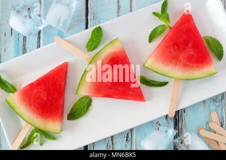 Gruppo di fetta di anguria popsicles su una piastra bianca con rustici blu sullo sfondo di legno Foto Stock