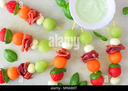 In estate gli spiedini di frutta con melone, formaggio e prosciutto, sopra visualizza su un marmo bianco sullo sfondo Foto Stock