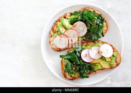 Piastra di avocado toast con cavoli rapa e ravanelli su tutto il pane di grano, vista dall'alto su un Sfondo marmo Foto Stock