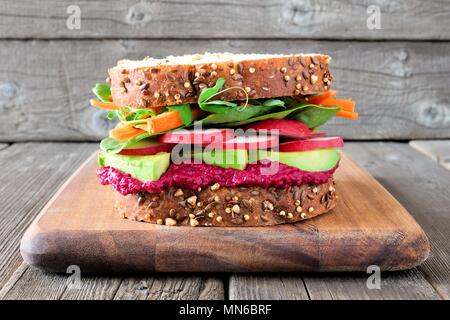 Super sandwich con barbabietole hummus, avocado, ortaggi e verdure e su tutto il pane di grano contro uno sfondo di legno Foto Stock