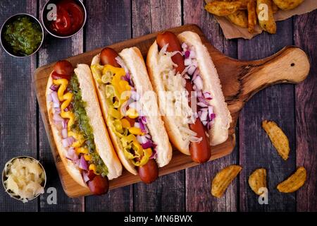 Hot Dogs completamente caricato con farciture assortite su un dispositivo di compressione scheda, scena di overhead Foto Stock