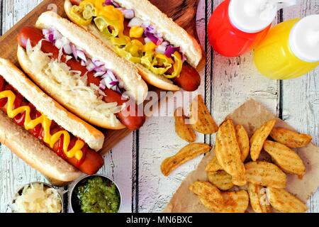 Hot Dogs con assortimento di condimenti e Spicchi di patate sopra visualizza su un rustico di legno bianco sullo sfondo Foto Stock
