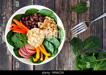 Pranzo sano ciotola con la quinoa, hummus e verdure miste, overhead scena su un rustico sfondo legno Foto Stock