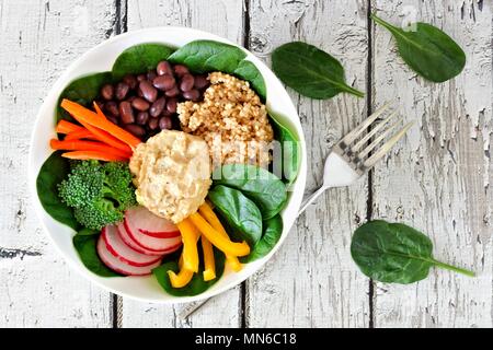Pranzo sano ciotola con la quinoa, hummus e verdure miste, overhead di scena sul legno bianco Foto Stock