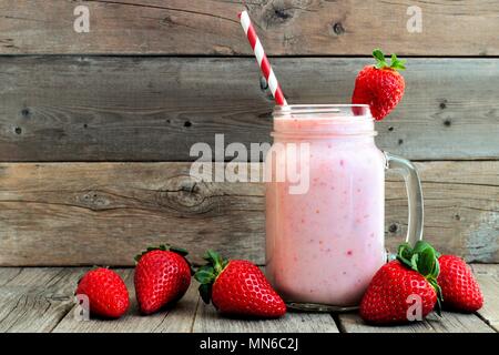 Un sano frullato fragole in un massone un vasetto di vetro con bacche sparse su un rustico sfondo legno Foto Stock