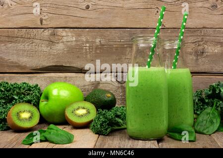 Frullato di verde in bottiglie di latte con kale, avocado, spinaci, mela e kiwi contro un rustico sfondo di legno Foto Stock