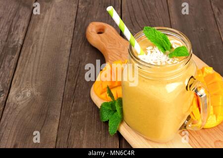 Mango frullato di cocco in una giara di mason vetro sulla scheda di racchetta contro un rustico sfondo legno Foto Stock