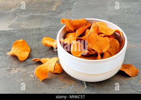 Ciotola di dolci sani potato chips su un sfondo di ardesia Foto Stock