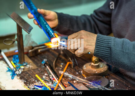 Le mani dell'artigianato uomo che fa un oggetto di vetro presso la fiera di artigianato.produttore di vetro lavorando il vetro fuso con una torcia ardente. In prossimità di fiamme da bl Foto Stock