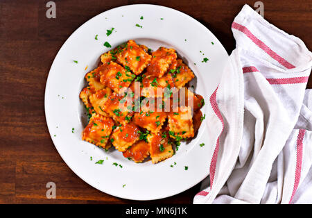 Ravioli freschi di pasta con il prezzemolo e la foglia di basilico, cucina italiana. Piastra bianca e tavolo in legno, piatto di pasta. Foto Stock