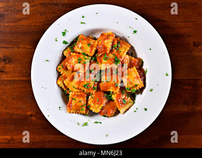 Ravioli freschi di pasta con il prezzemolo e la foglia di basilico, cucina italiana. Piastra bianca e tavolo in legno, piatto di pasta. Foto Stock