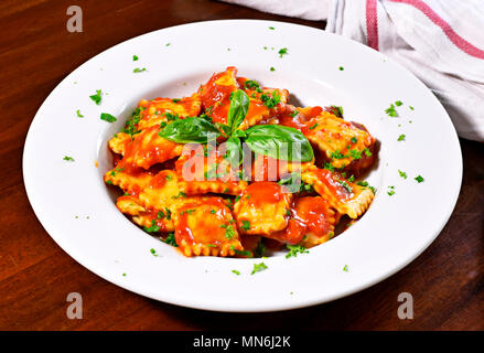 Ravioli freschi di pasta con il prezzemolo e la foglia di basilico, cucina italiana. Piastra bianca e tavolo in legno, piatto di pasta. Foto Stock
