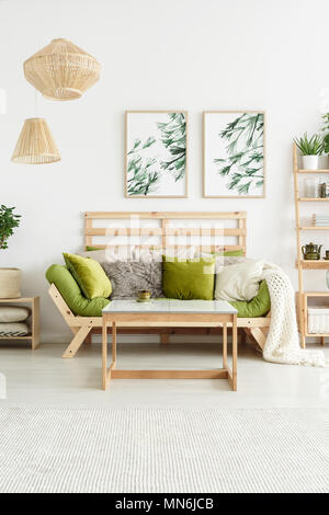Poster con piante pendenti sul muro bianco in un elegante salotto interno verde con salotto e tavolo in legno Foto Stock
