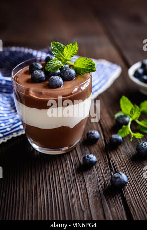 Layered cioccolato e vaniglia dessert mascarpone guarnita con mirtillo, servita in un vasetto di vetro Foto Stock