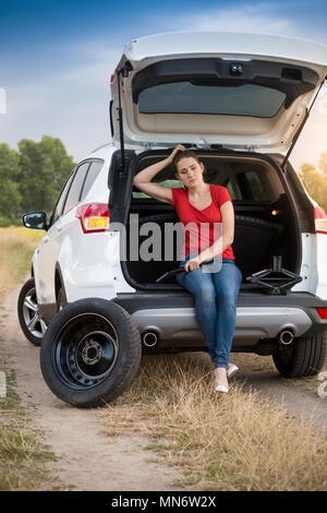 Giovane donna seduta in open baule auto in attesa per il servizio automatico per cambiare il pneumatico sgonfio Foto Stock