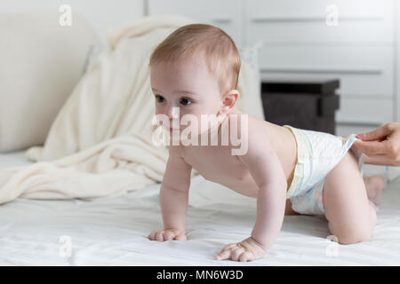 Carino 9 mesi baby boy in pannolini strisciando sul letto Foto Stock