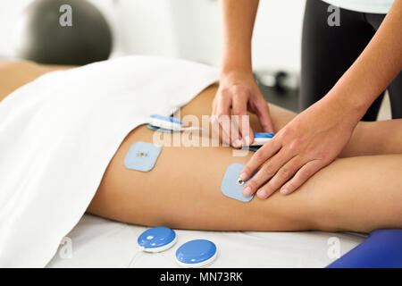 Fisioterapista applicazione di elettrostimolazione in terapia fisica ad una giovane donna. Visita medica di controllo presso la gamba in un centro di fisioterapia. Foto Stock