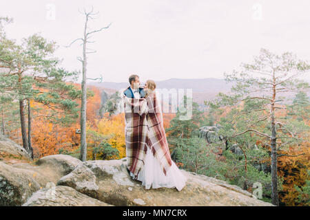 La foto in orizzontale della sposa giovane avvolto in maglia plaid in piedi sulle rocce. Foto Stock