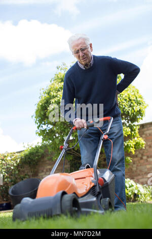 Senior uomo che soffre di mal di schiena mentre mediante elettropompa Tosaerba per taglio di erba a casa Foto Stock