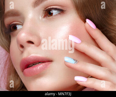 Bellissima ragazza con la luce per il make-up e manicure dolce in abiti rosa. Bellezza viso. Il design dei chiodi. Foto Stock