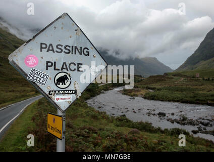 Un passante posto cartello stradale in una singola corsia strada oltre il Fiume Coe in Glen Coe sfigurata con adesivi Foto Stock